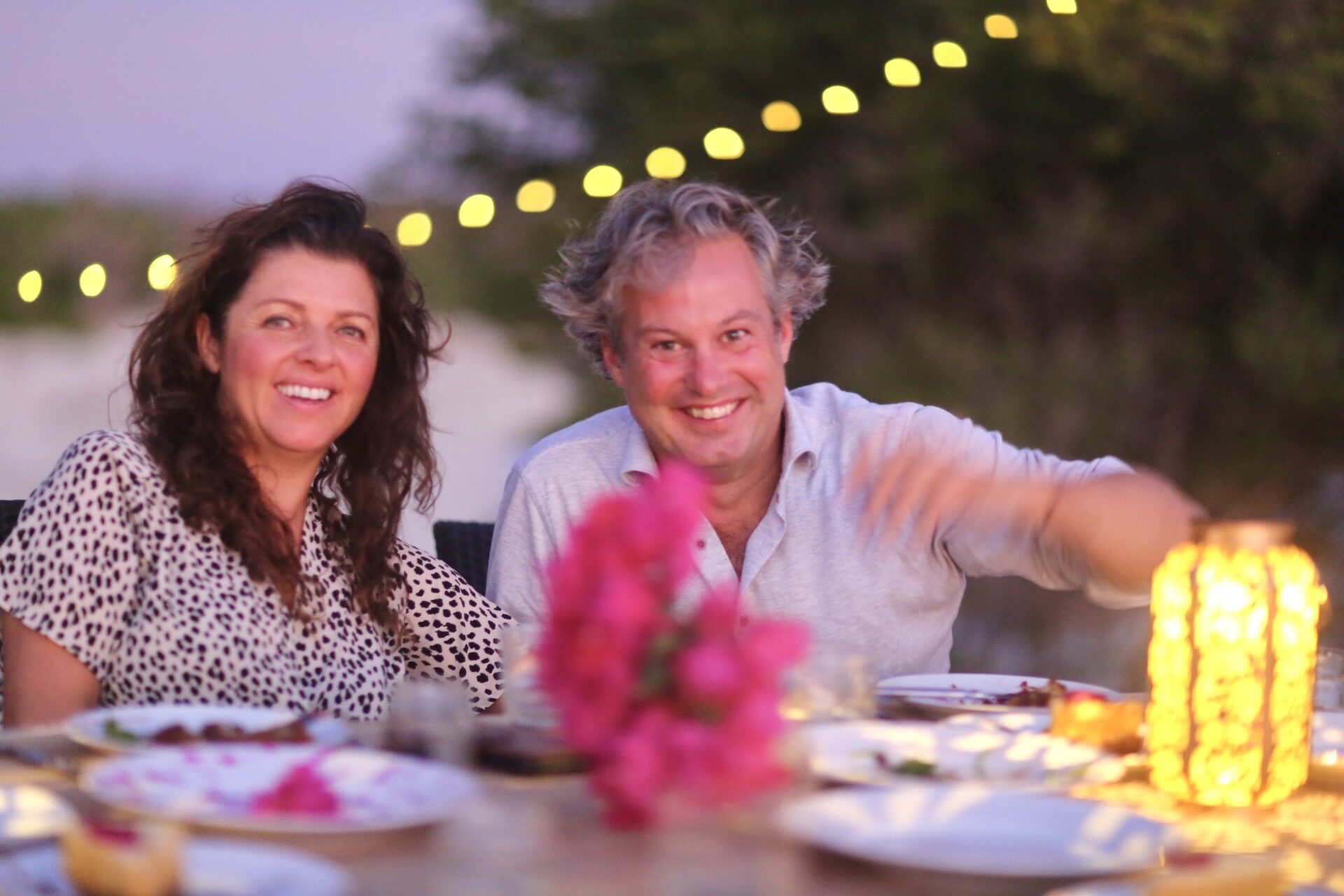 A couple dining under string lights at dusk